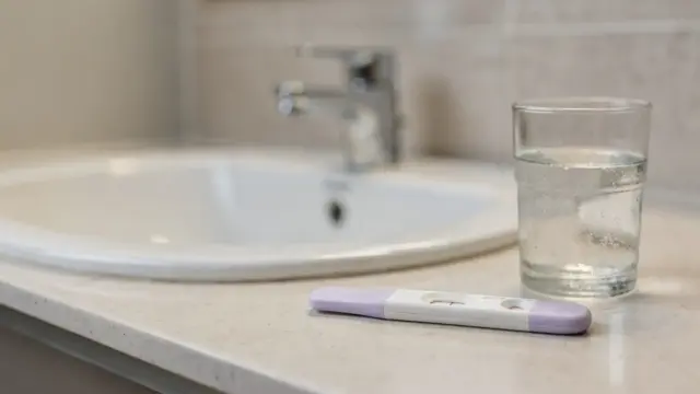 Schwangerschaftstest mit Wasser neben einem Glas in einem Badezimmer
