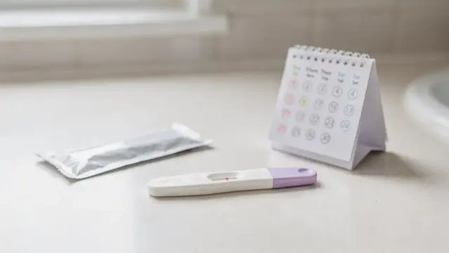 Schwangerschaftstest auf einem Badezimmerregal mit Kalender und zweitem Test zur Wiederholung
