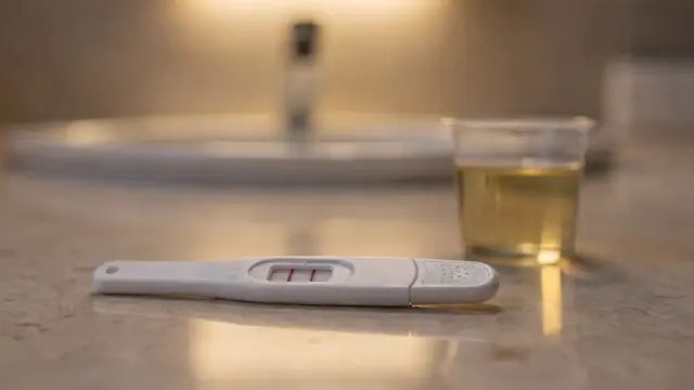 Schwangerschaftstest mit Abendurin auf einem Badezimmerregal neben einem Probenbecher
