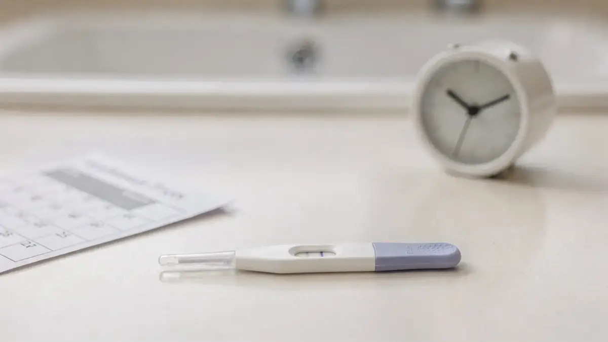 Schwangerschaftstest auf dem Badregal mit Kalender und Uhr zum Thema Test vor der Periode