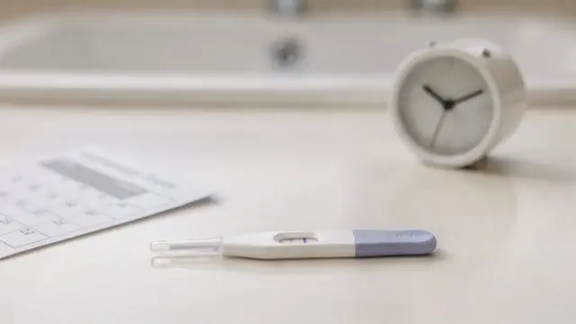 Schwangerschaftstest auf dem Badregal mit Kalender und Uhr zum Thema Test vor der Periode