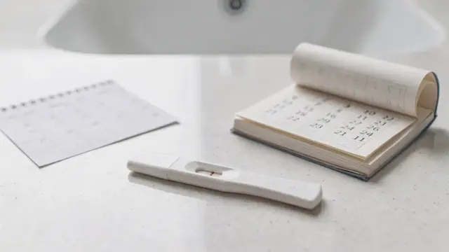 Negativer Frühtest neben Kalender und Notizblock zum Thema ausbleibende Periode